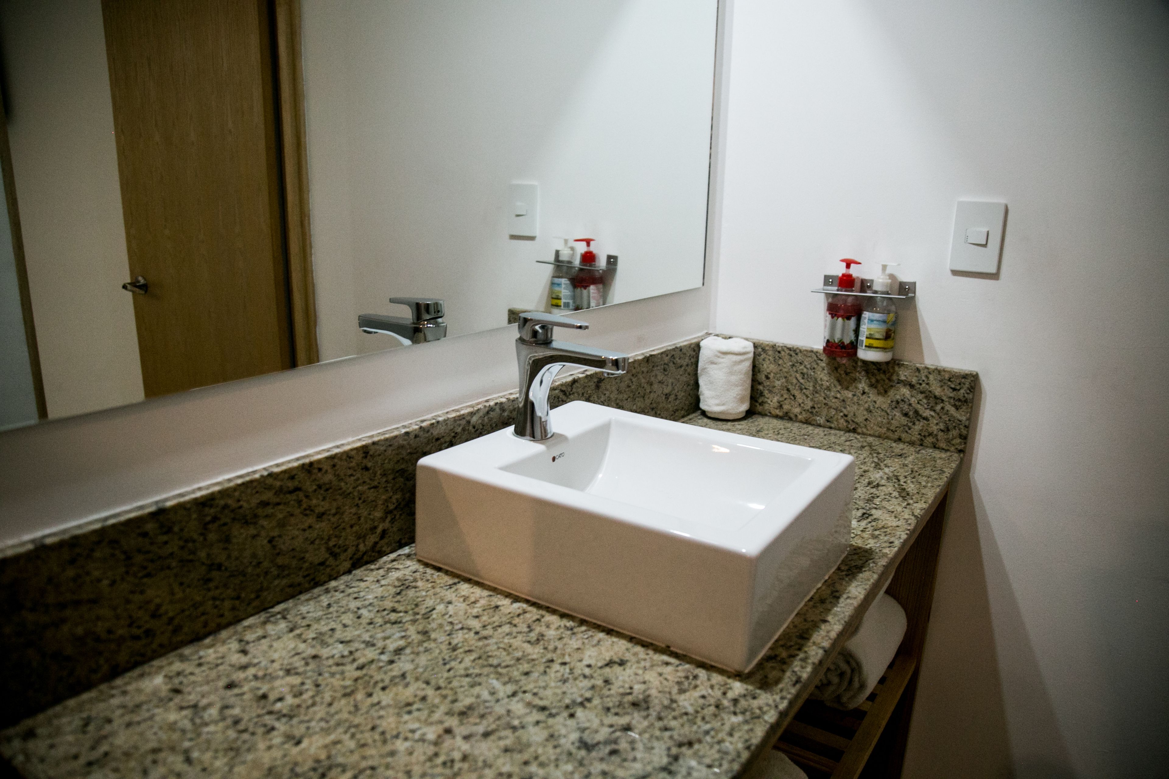 Une salle de bain avec un lavabo rectangulaire, un comptoir en granit et un grand miroir.