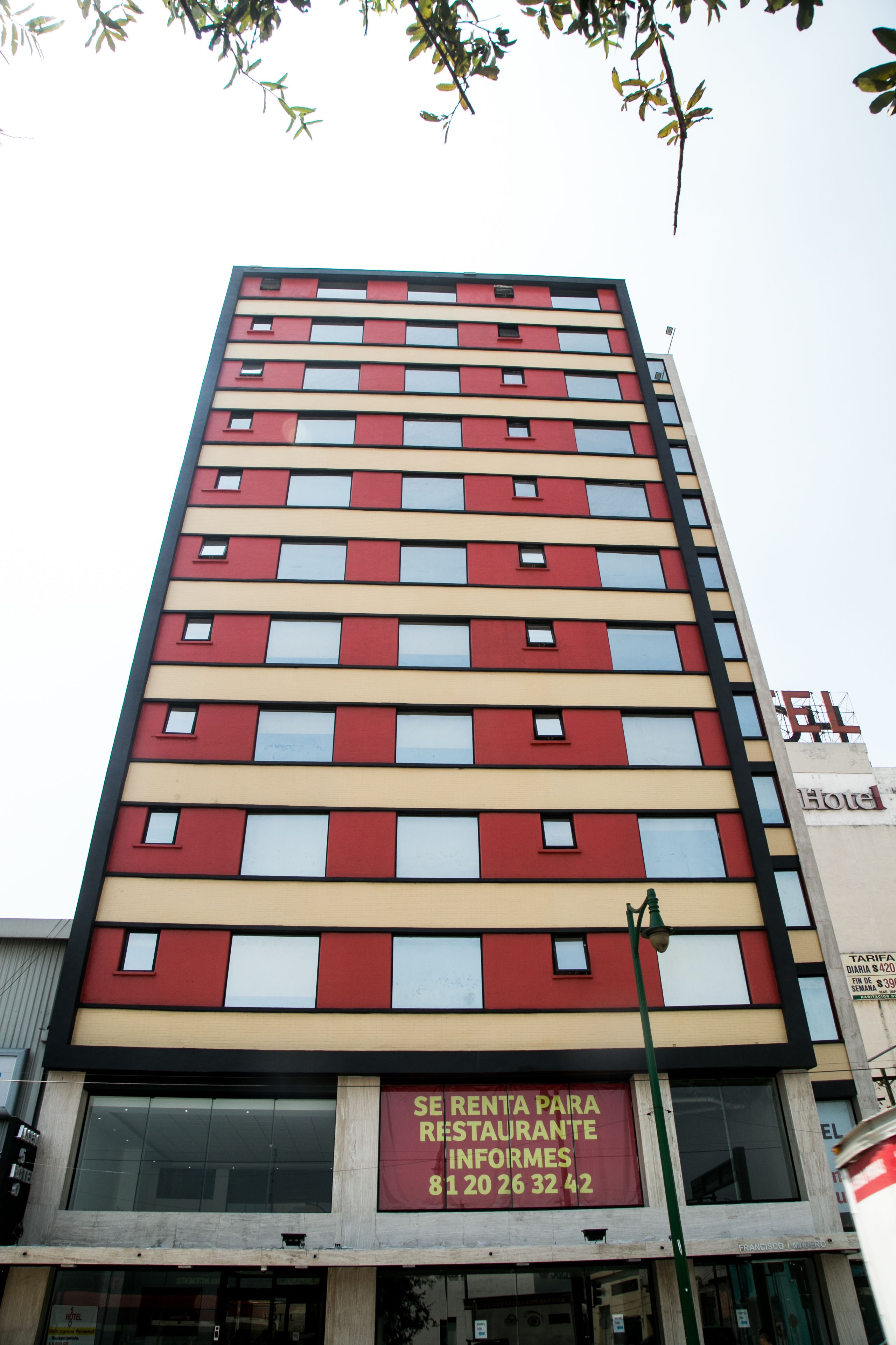 Un hôtel à plusieurs étages, doté d’une façade rouge et beige, de grandes fenêtres et d’une enseigne indiquant la location de chambres.