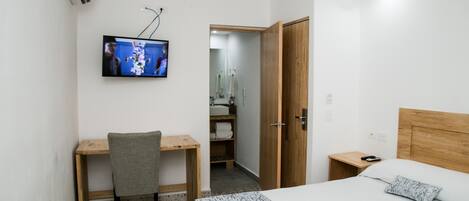 Habitación de hotel con cama, escritorio, silla, televisor, armario y baño visible a través de una puerta abierta.
