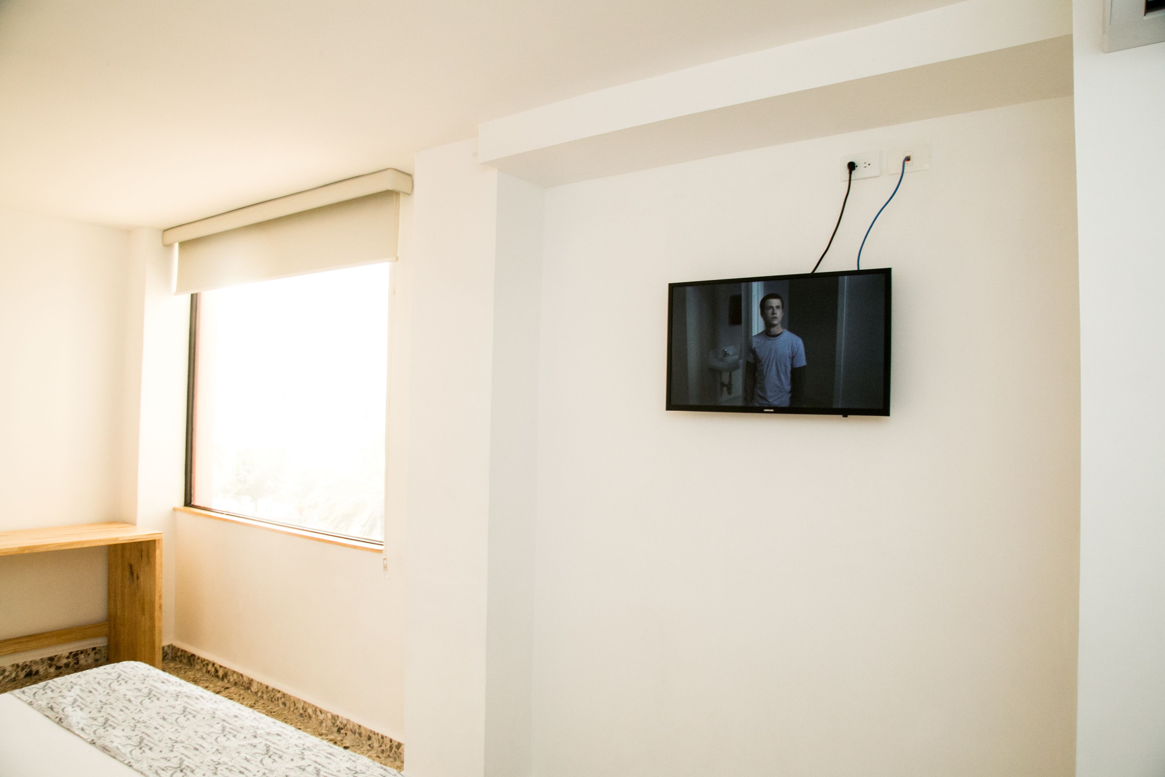 A bedroom with a bed, a window, and a mounted television.