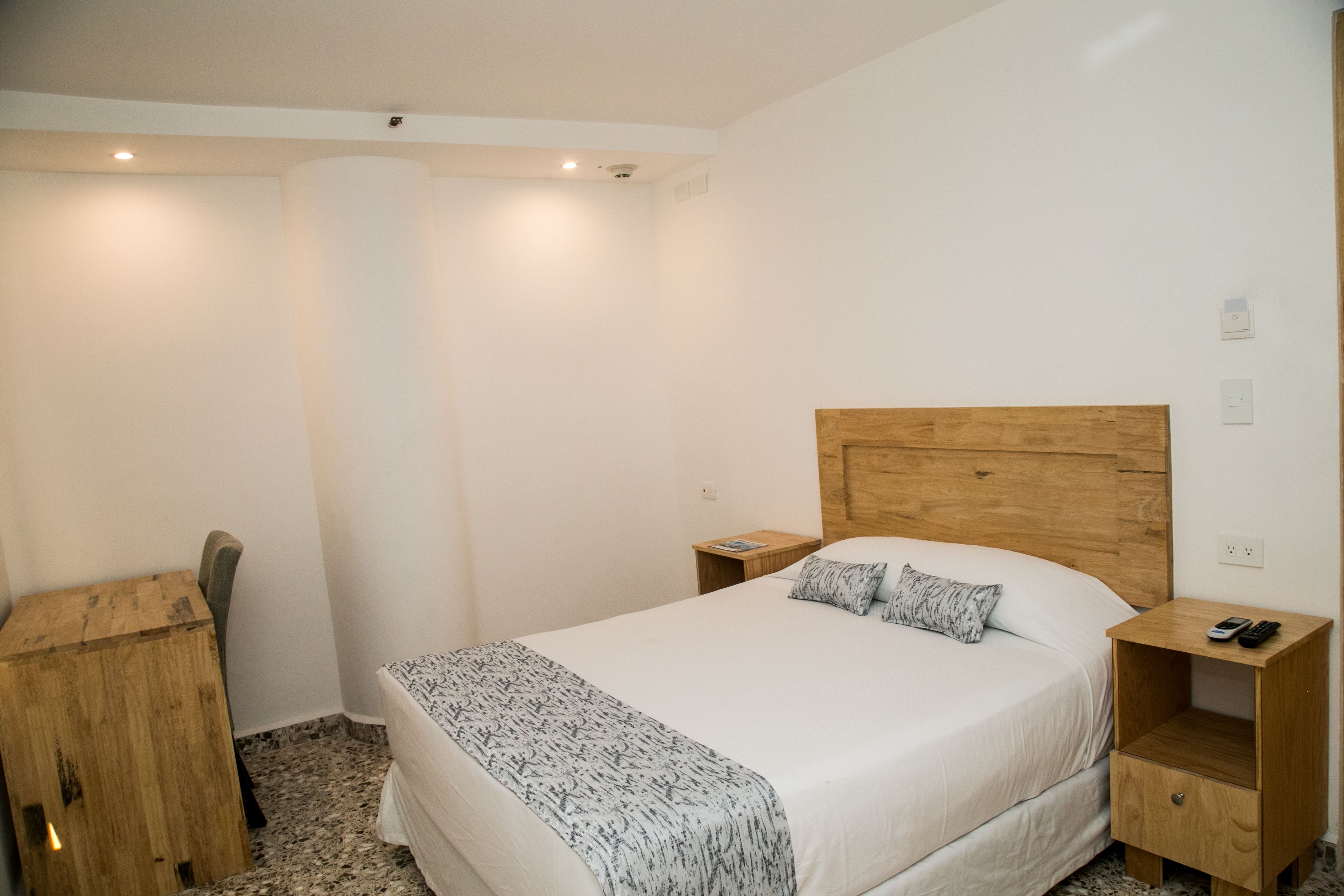 Een slaapkamer met een houten hoofdbord, een bed met witte beddengoed, een nachtkastje met een afstandsbediening en een klein houten nachtkastje.