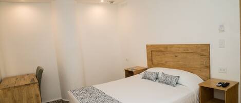 Een slaapkamer met een houten hoofdbord, een bed met witte beddengoed, een nachtkastje met een afstandsbediening en een klein houten nachtkastje.