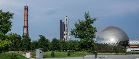 Un parque con una gran esfera metálica, una chimenea alta y un edificio de diseño peculiar.
