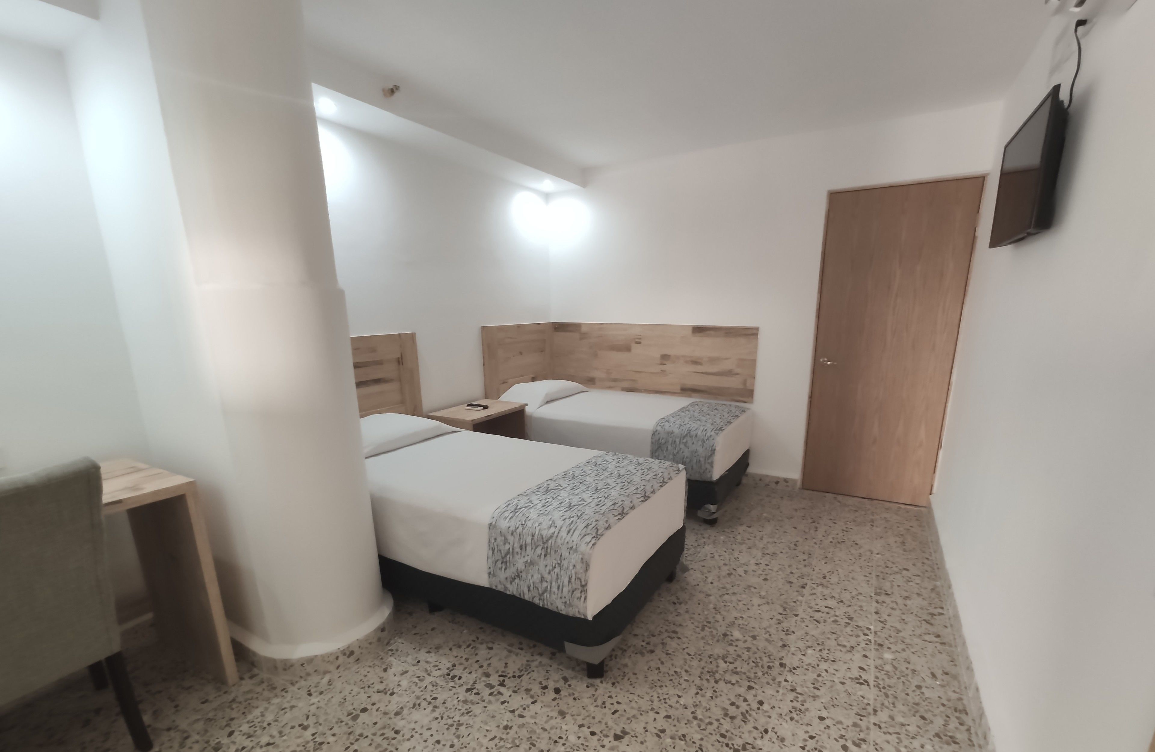 Une chambre d’hôtel avec deux lits, une tête de lit en bois, un petit bureau et un téléviseur fixé au mur.