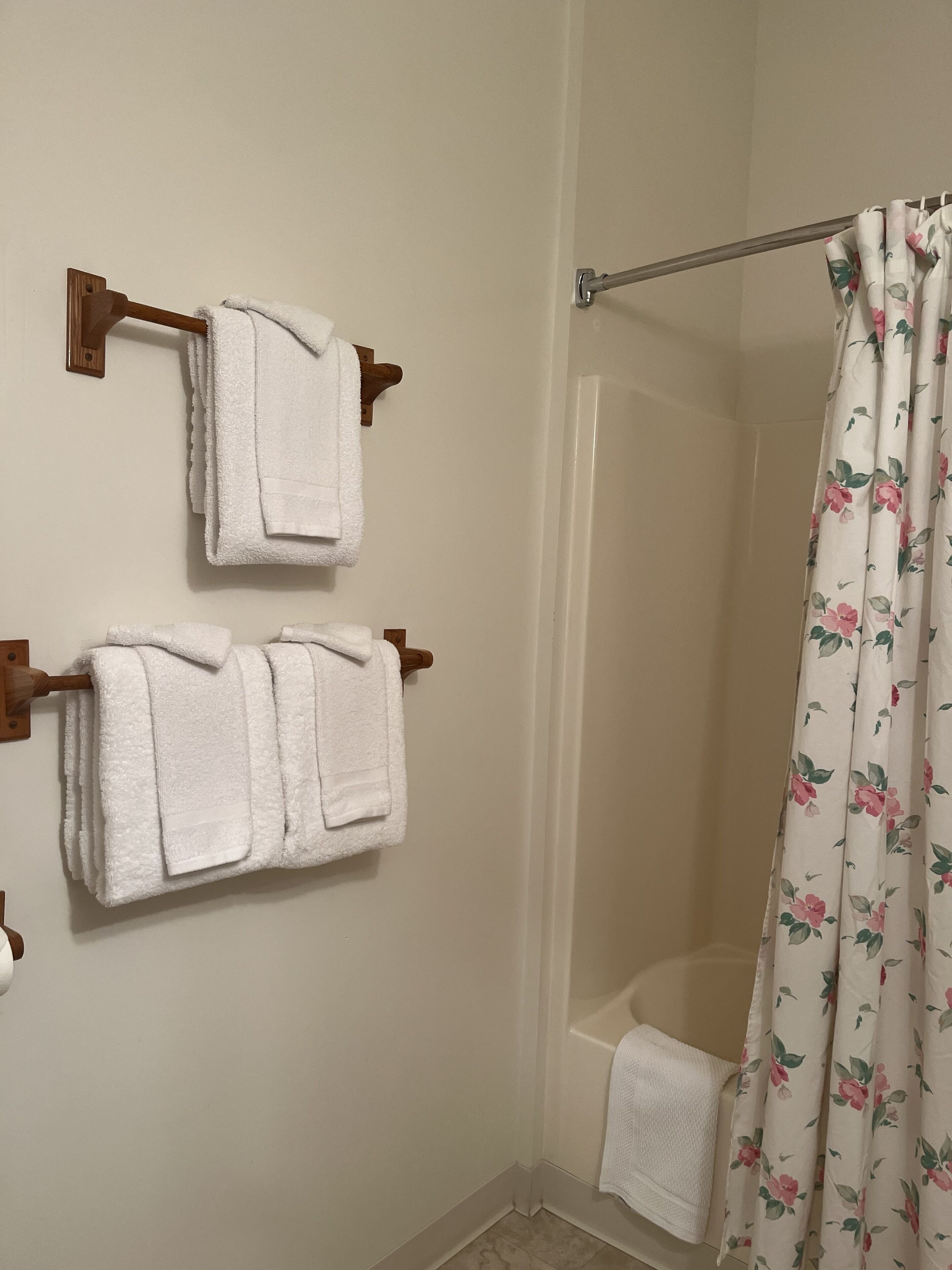 A bathroom with two white towels hanging on wooden towel racks, a shower curtain with a floral pattern, and a white bathtub.