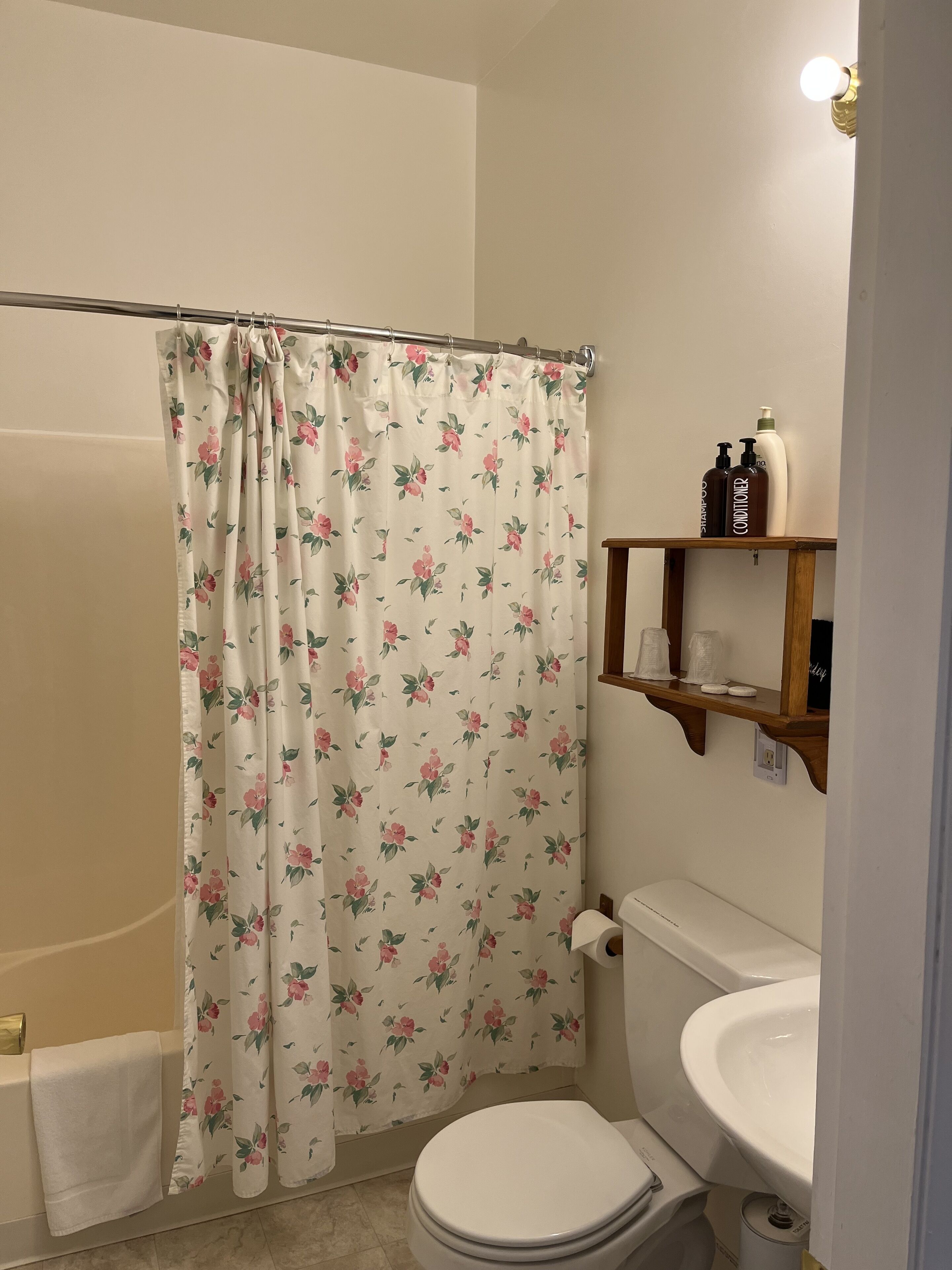 A bathroom with a shower curtain, toilet, sink, and a shelf with toiletries.