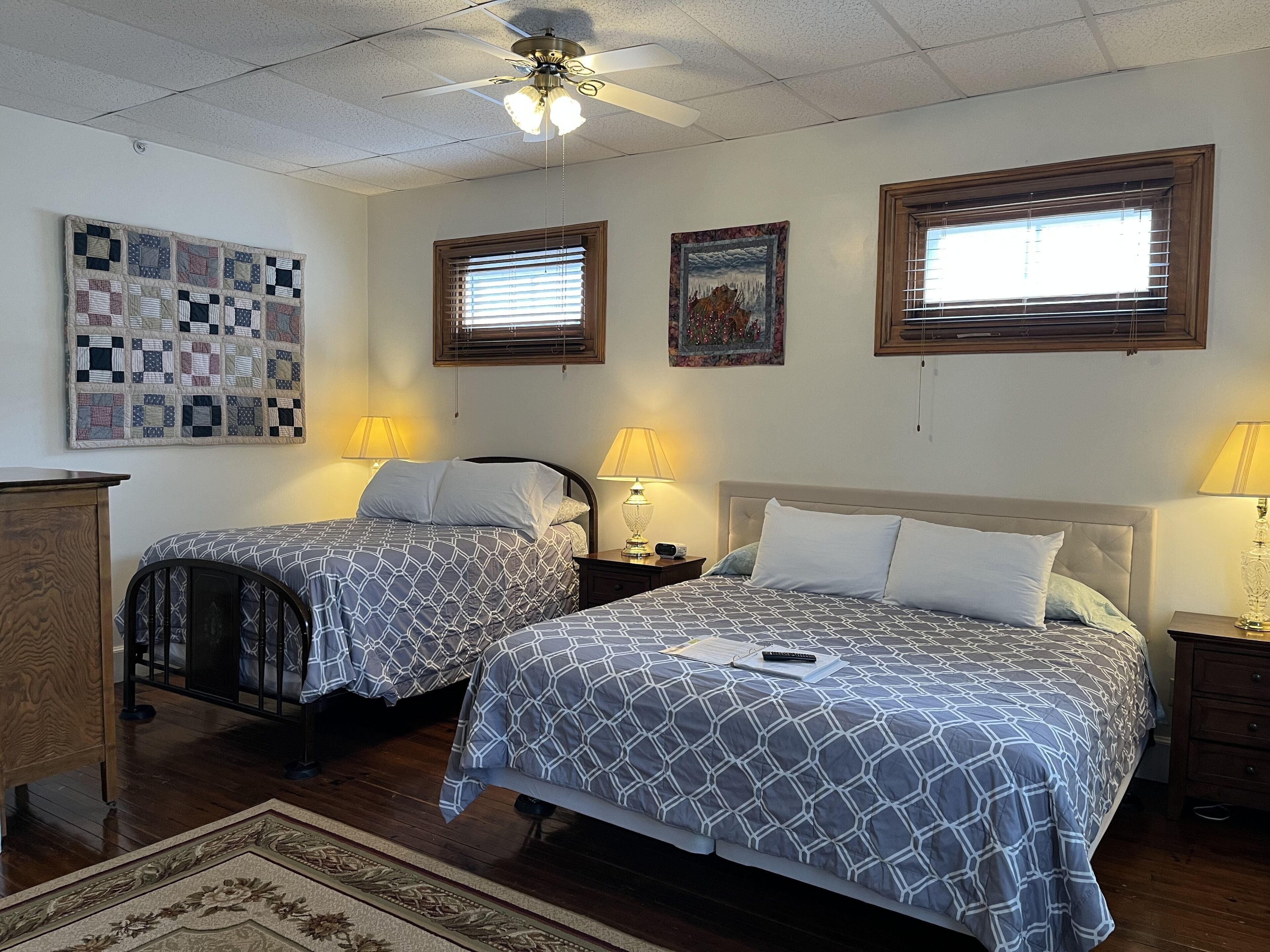 A room with two beds, a quilt, a wooden dresser, and a ceiling fan.