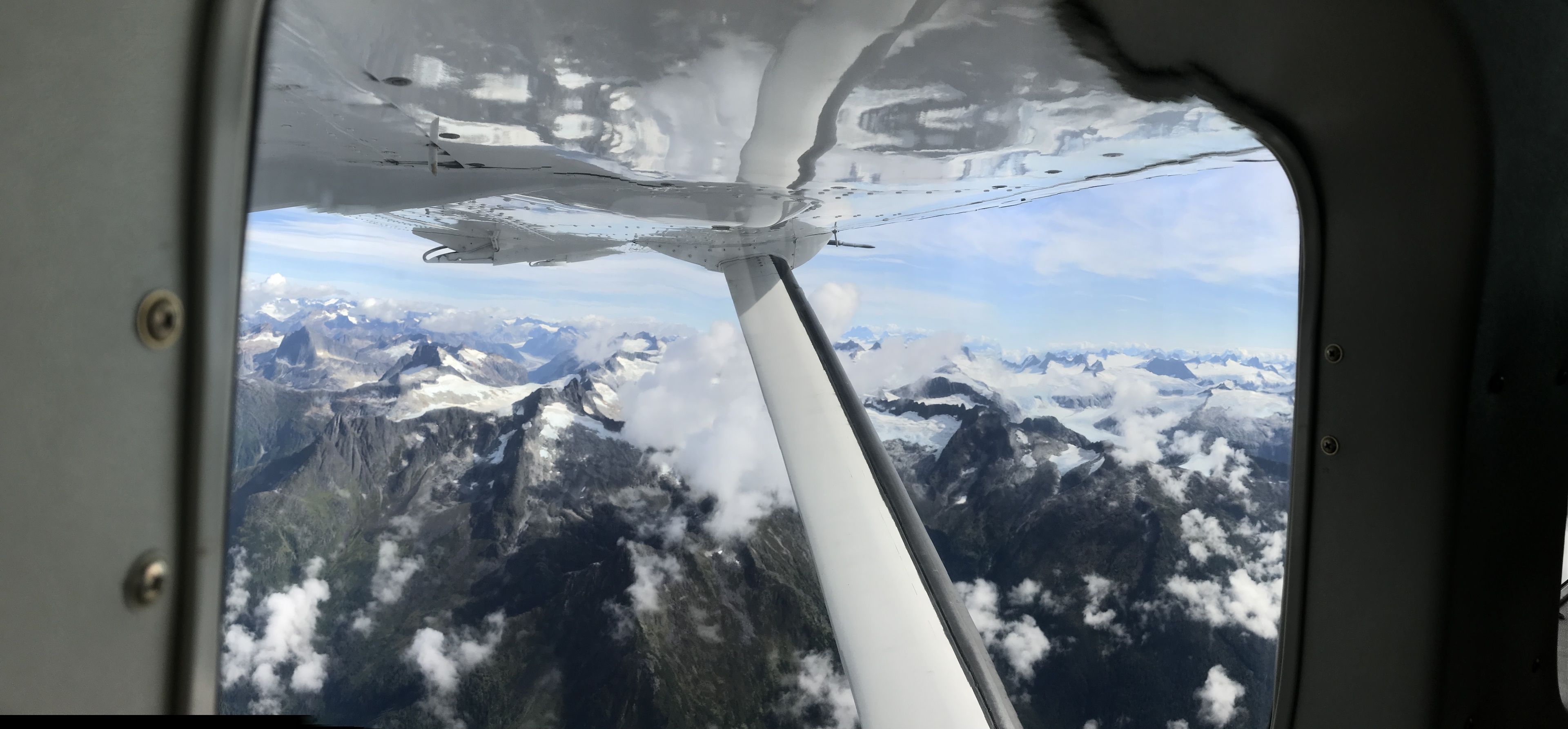 An airplane wing with a view of snow-capped mountains and clouds below.