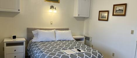 A neatly arranged bedroom with a bed, bedside tables, a nightstand, a wall-mounted light fixture, and framed pictures.