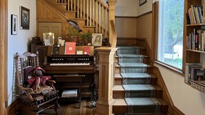 A grand staircase with ornate railings, a piano, and a bookshelf filled with books. - At the White House (Skagway)