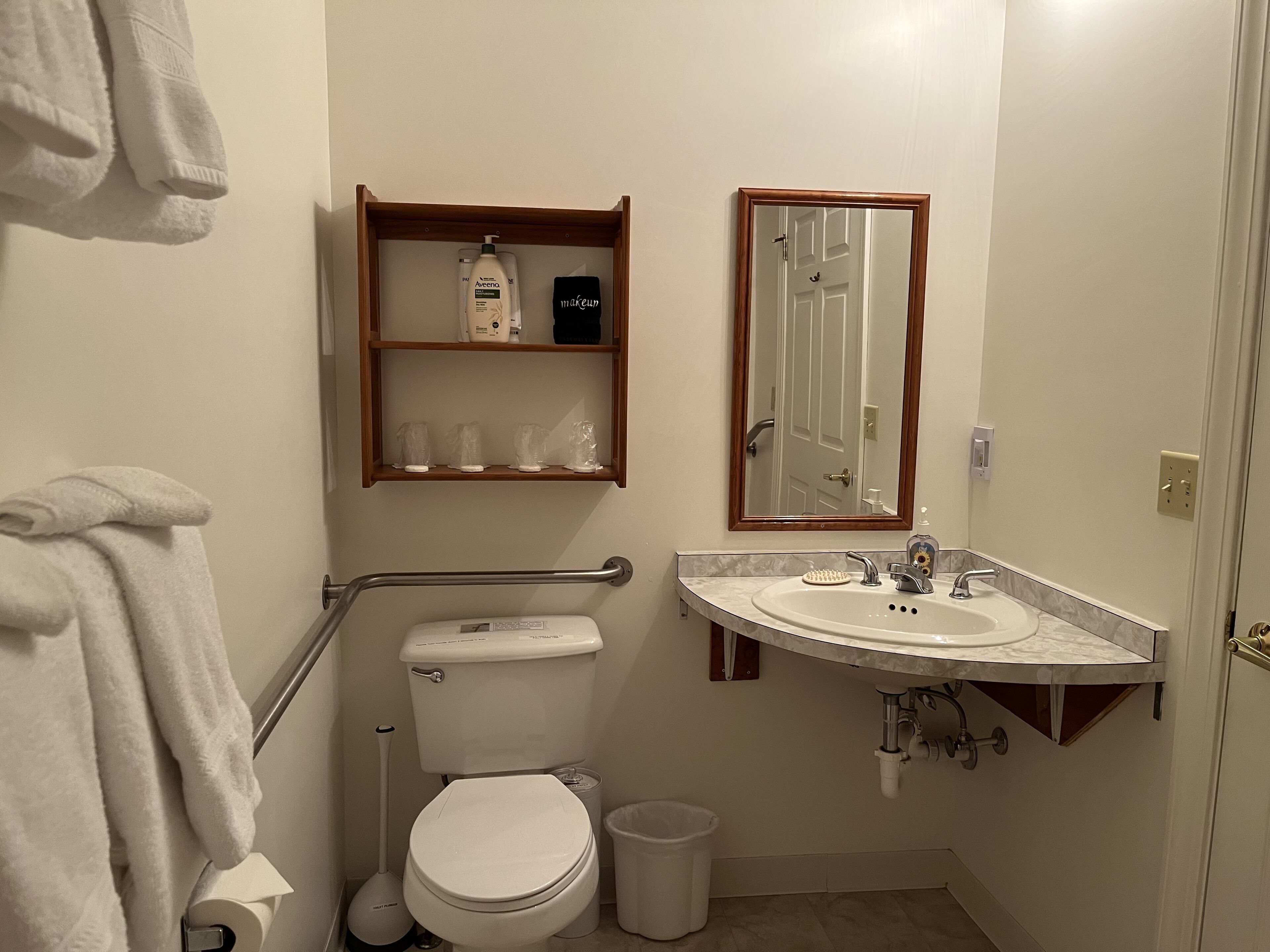 A bathroom with a toilet, sink, mirror, and a shelf with toiletries.