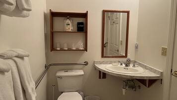 A bathroom with a toilet, sink, mirror, and a shelf with toiletries.