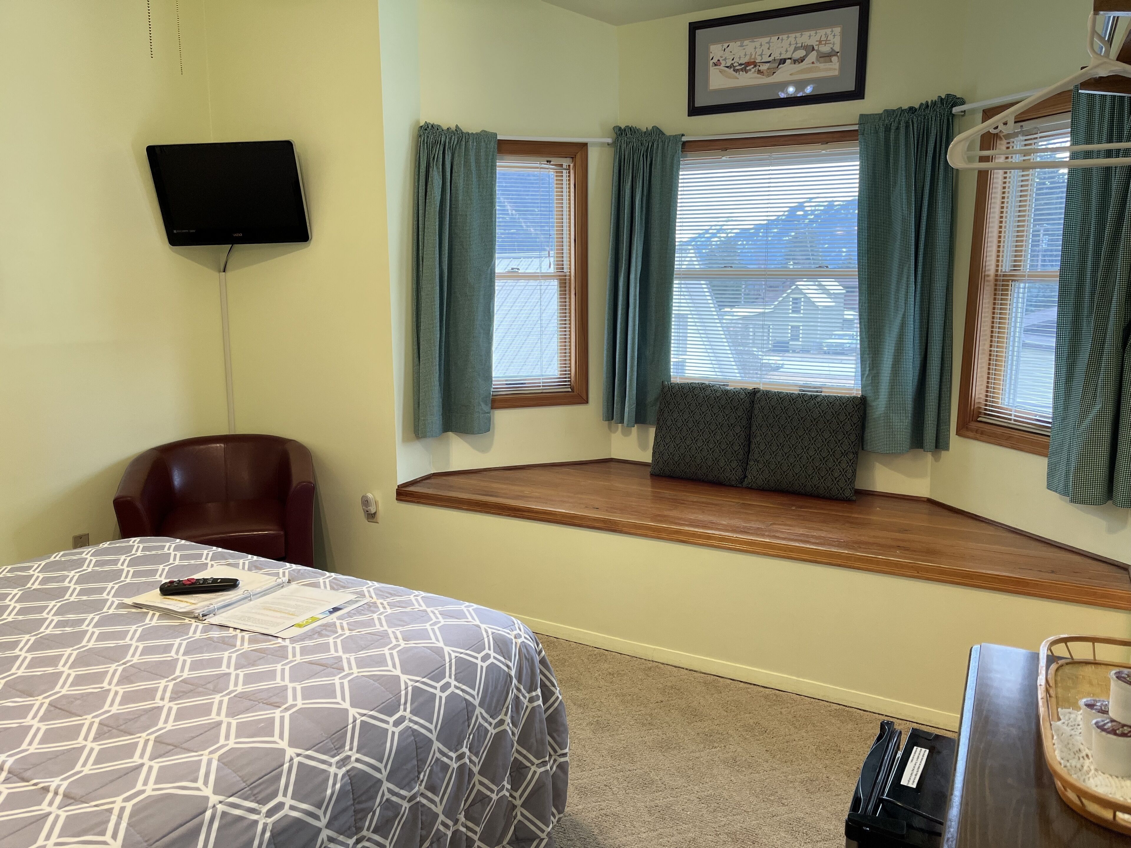 Habitación de hotel con cama, una silla, un asiento junto a la ventana con cortinas, televisor y una mesita con bandeja.