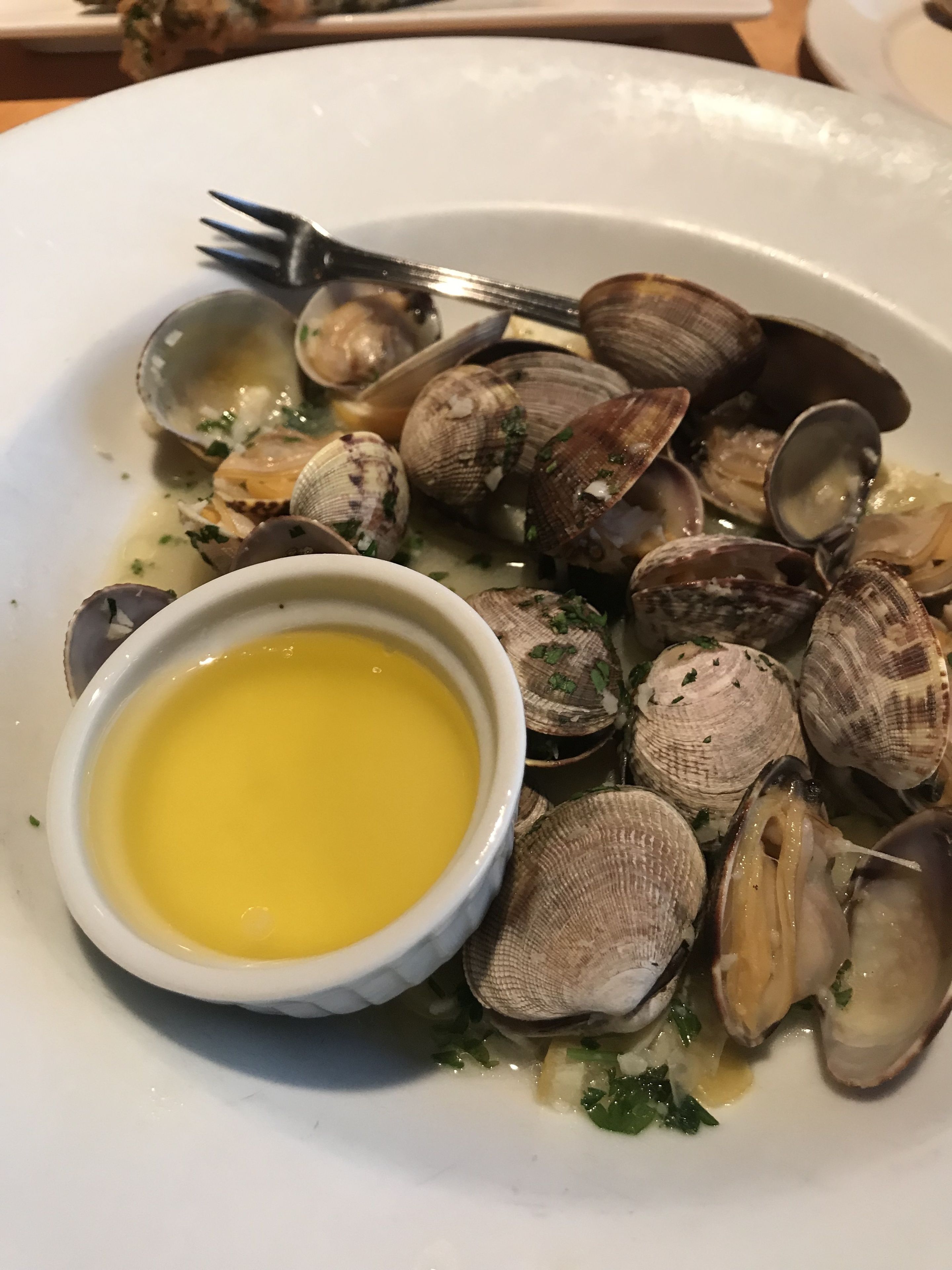 A plate of clams with a small bowl of butter and a fork.