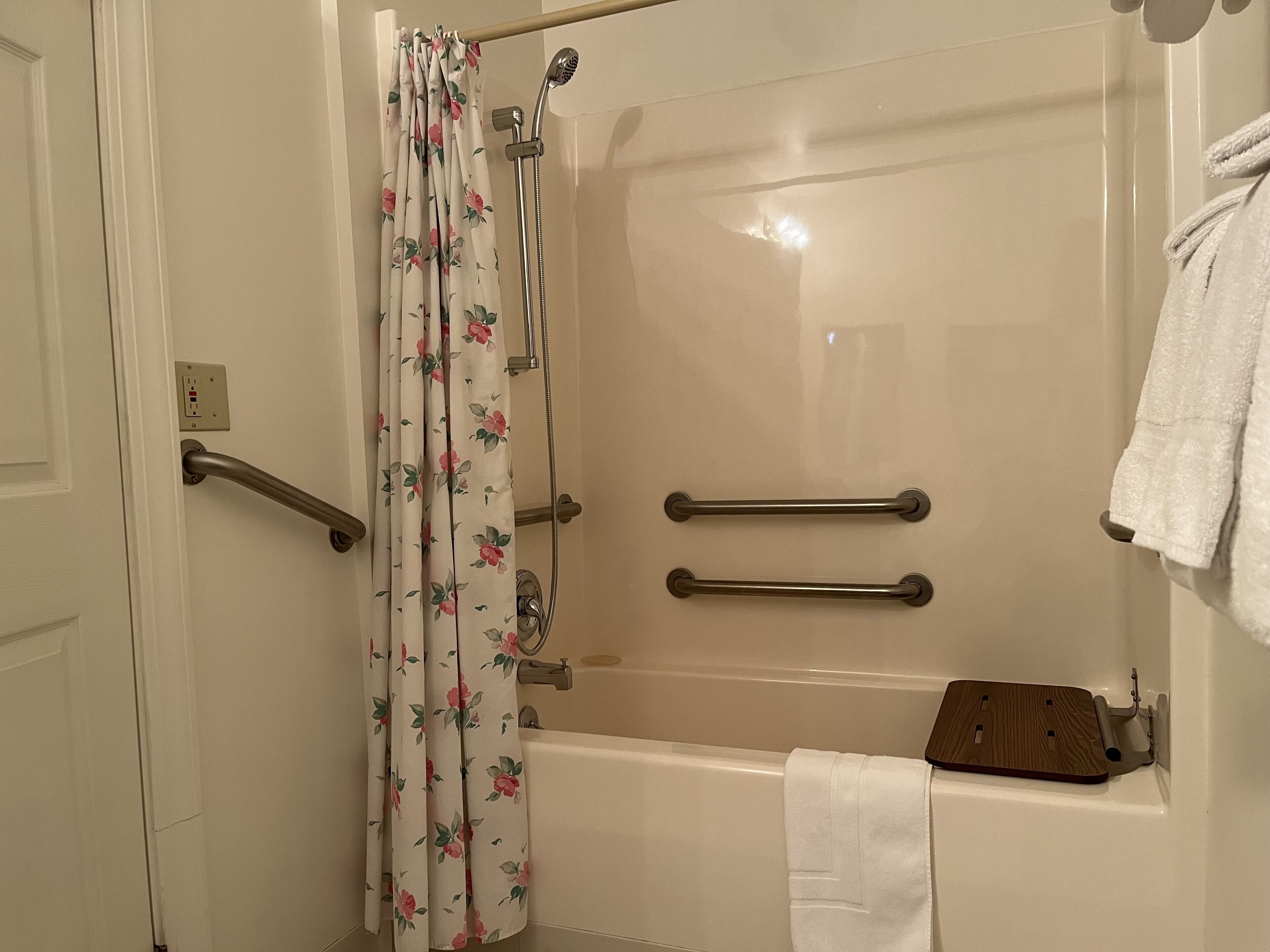 A bathroom with a bathtub, a shower, and a toilet. There are two grab bars installed for safety.