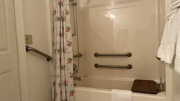 A bathroom with a bathtub, a shower, and a toilet. There are two grab bars installed for safety.