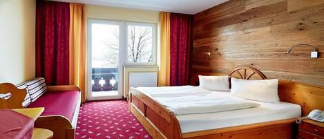 Ein Hotelzimmer mit einem Holzbett, einem Schreibtisch mit Stuhl, einem kleinen Tisch und Blick aus dem Fenster.
