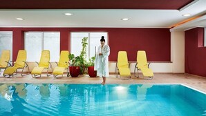 An indoor swimming pool with yellow lounge chairs and a person in a white robe standing by the pool. - Hotel Wieser (Mittersill)