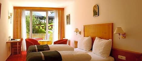 A hotel room with a bed, two chairs, a small table, and a view of greenery through the window.