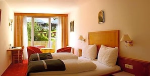 A hotel room with a bed, two chairs, a small table, and a view of greenery through the window.