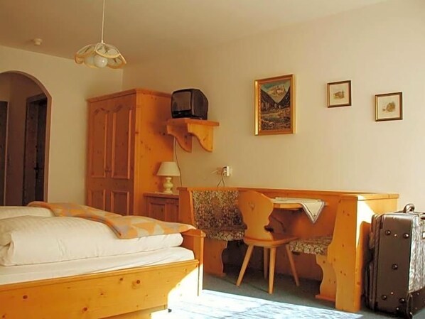 A bedroom with a bed, a desk, a chair, a suitcase, and a television.
