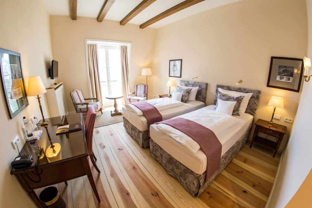 A hotel room with two beds, a desk, a chair, and a window with curtains.