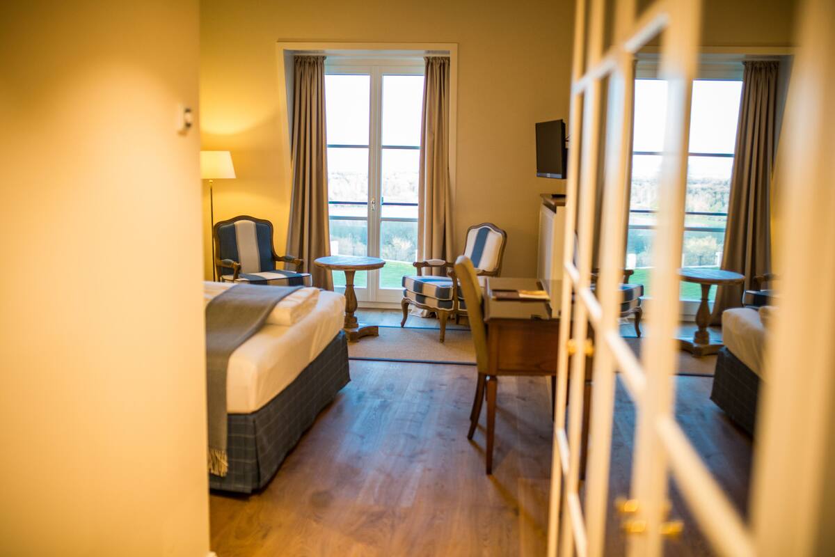 A hotel room with a bed, a desk, a chair, a TV, and a window with curtains.