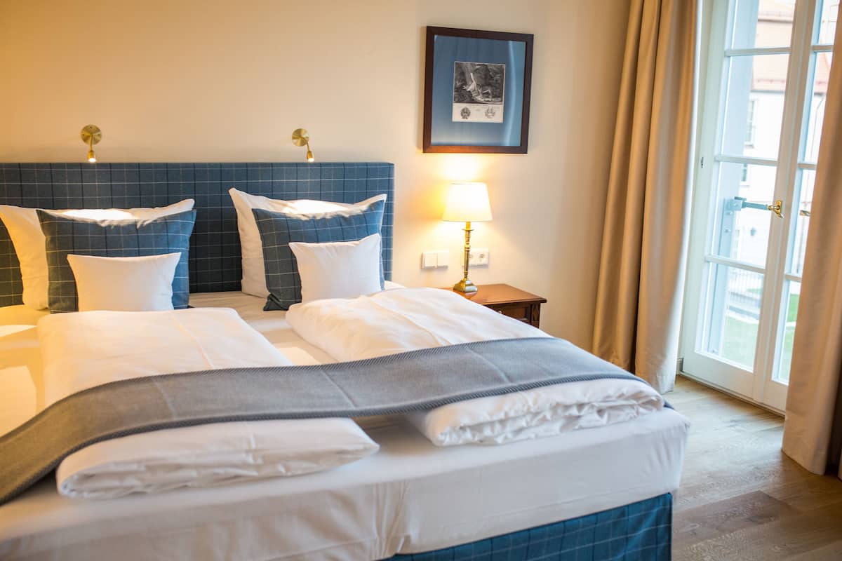 A hotel room with a large bed, a bedside table with a lamp, a framed picture on the wall, and a window with curtains.