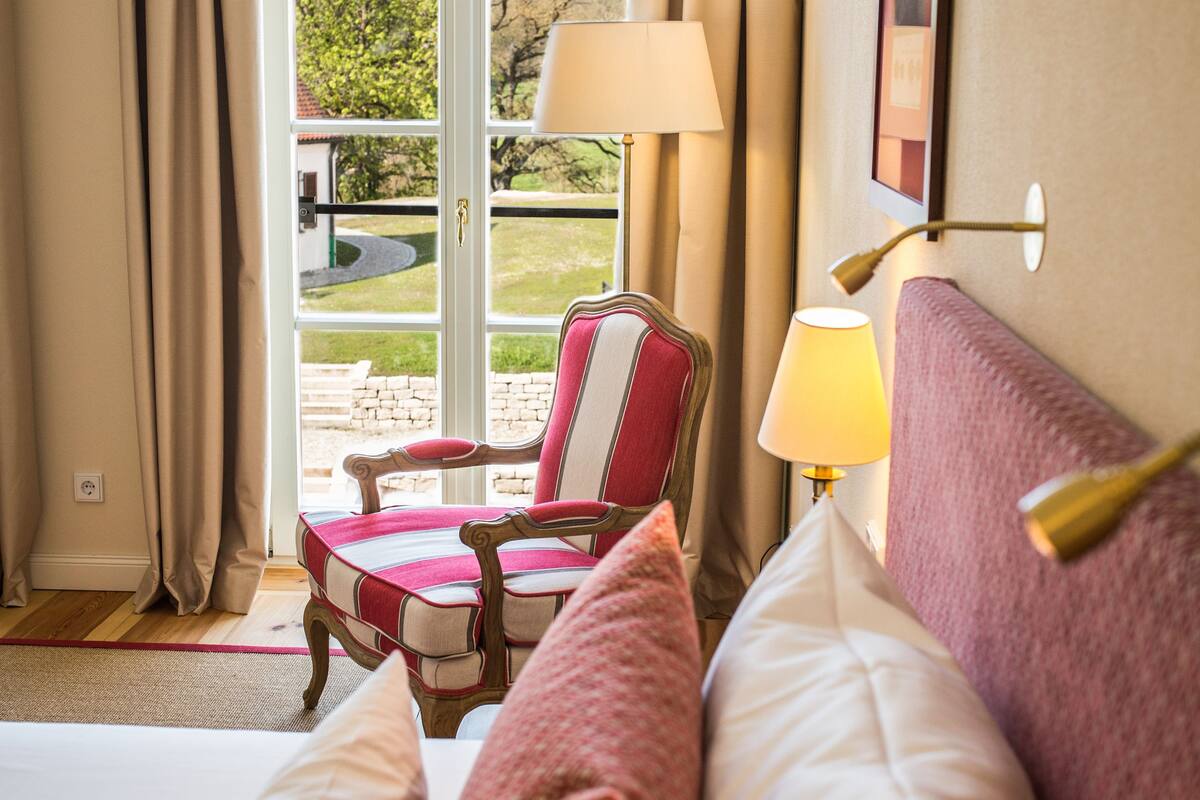 A hotel room with a bed, a chair, a lamp, and a view of the outdoors through a glass door.