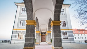 Un edificio con una entrada central enmarcada por columnas de piedra y un camino de ladrillo rojo que conduce a ella.