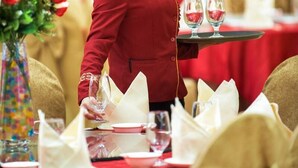 A person in a red uniform setting a table with white napkins and glassware. - Vienna Hotel (Shenzhen)