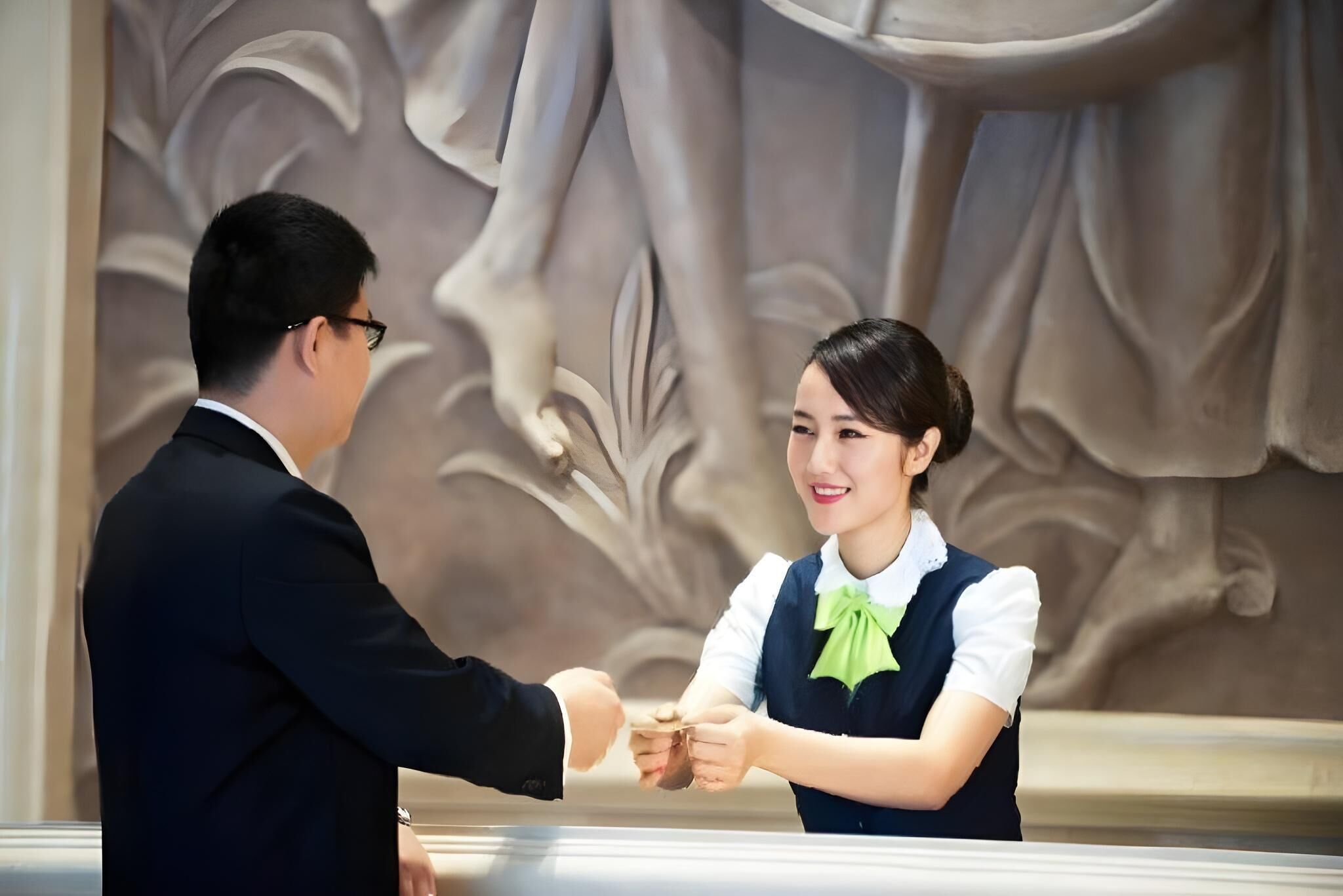 A handshake between two individuals in a formal setting with a decorative wall in the background.