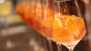 Un bar con copas de cóctel, gajos de naranja, una cuña de limón y una botella de líquido rojo siendo vertido.