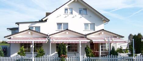 A two-story house with a white picket fence, a red and white striped awning over the entrance, and a sign that reads "Sperrheim."