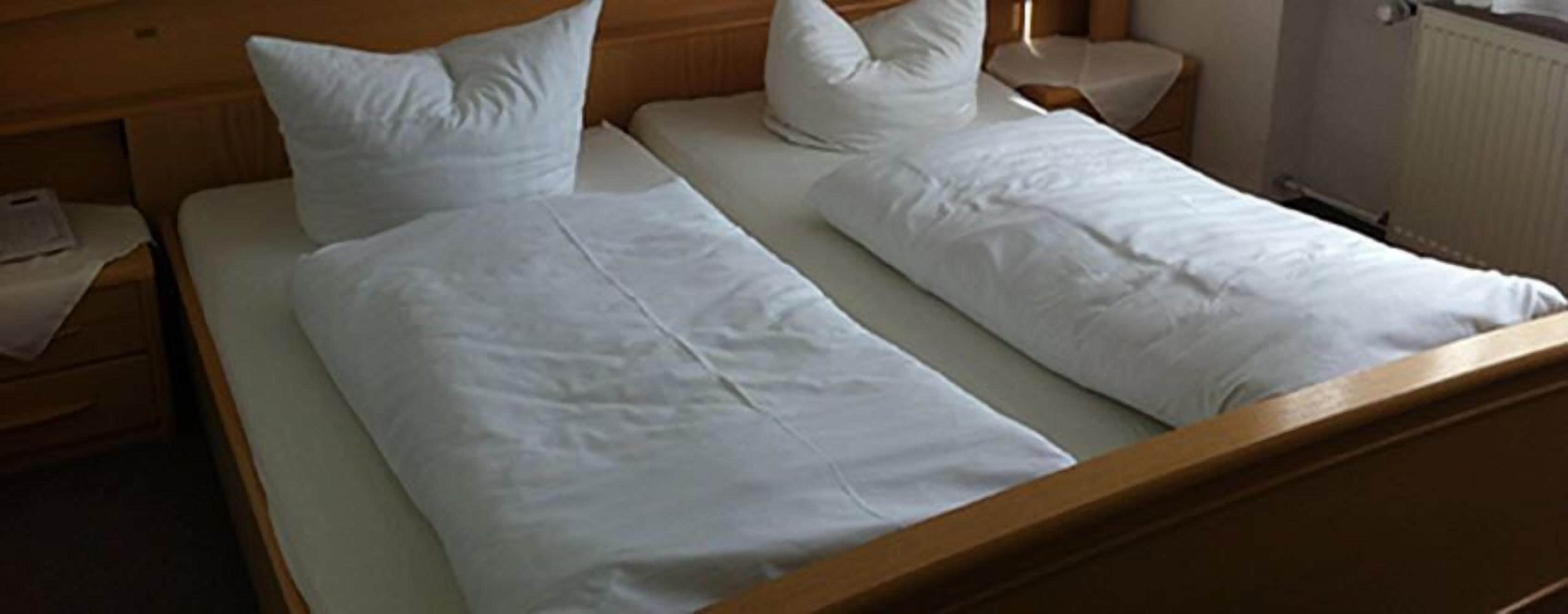 A double bed with white linens and pillows in a hotel room.