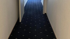 Un pasillo estrecho con una alfombra estampada que conduce a una puerta con un letrero de salida de emergencia encima.