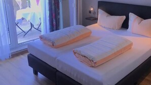 Un dormitorio con cama, almohadas, una mesita de noche con lámpara y vistas a través de un ventanal.