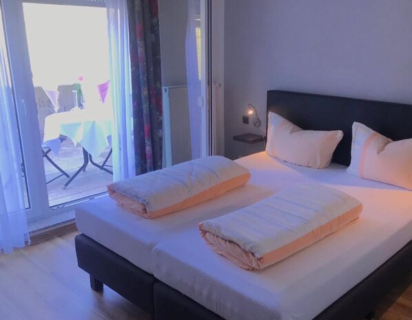 A bedroom with a bed, pillows, a bedside table with a lamp, and a view through a glass door. - Hotel am Kirschberg (Buseck)