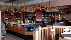 Zona de bar con estantes de madera llenos de botellas, una barra con una computadora portátil, y una persona trabajando detrás.