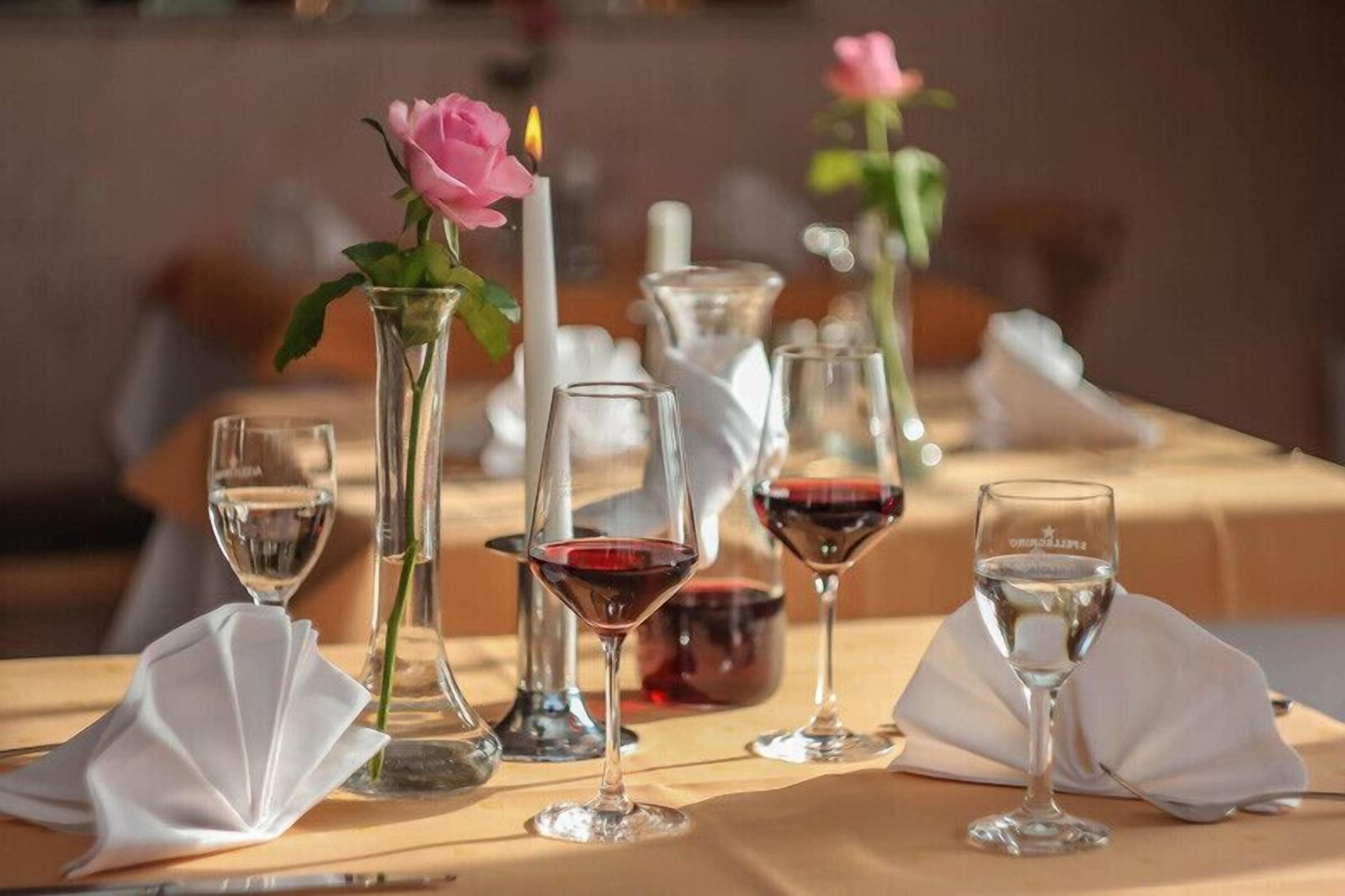 A dining table set with wine glasses, a candle, and a rose in a vase.