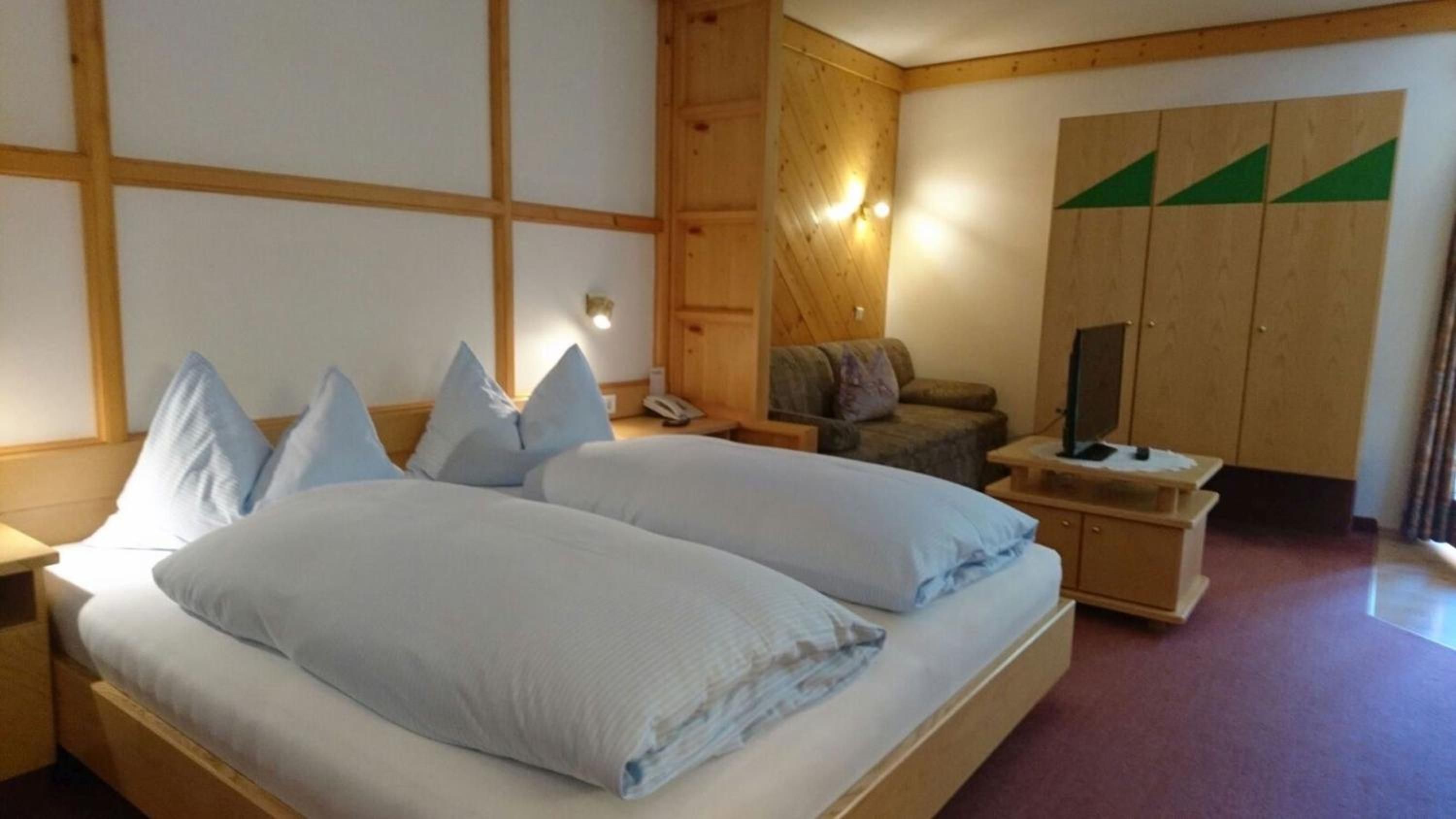 Ein Schlafzimmer mit einem großen Bett, einem Holzschrank, einer kleinen Couch und einem Fernseher auf einem Holztisch.