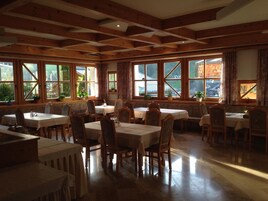 Comedor con vigas de madera, ventanas amplias y mesas dispuestas para comer.