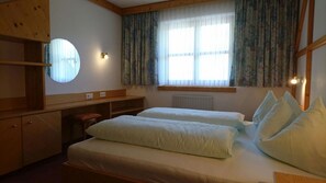 A room with two beds, a wooden desk, a round mirror, and a window with curtains.