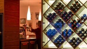 A restaurant with a wine rack displaying various bottles, a table with glasses and a candle, and a person working at the bar. - Trend Hotel (Banzkow)
