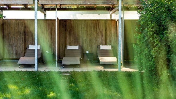 A covered outdoor seating area with three lounge chairs and a wooden fence backdrop. - Trend Hotel (Banzkow)