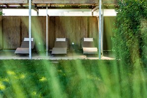 Un espacio de estar al aire libre cubierto con tres sillones reclinables y un cerco de madera al fondo.