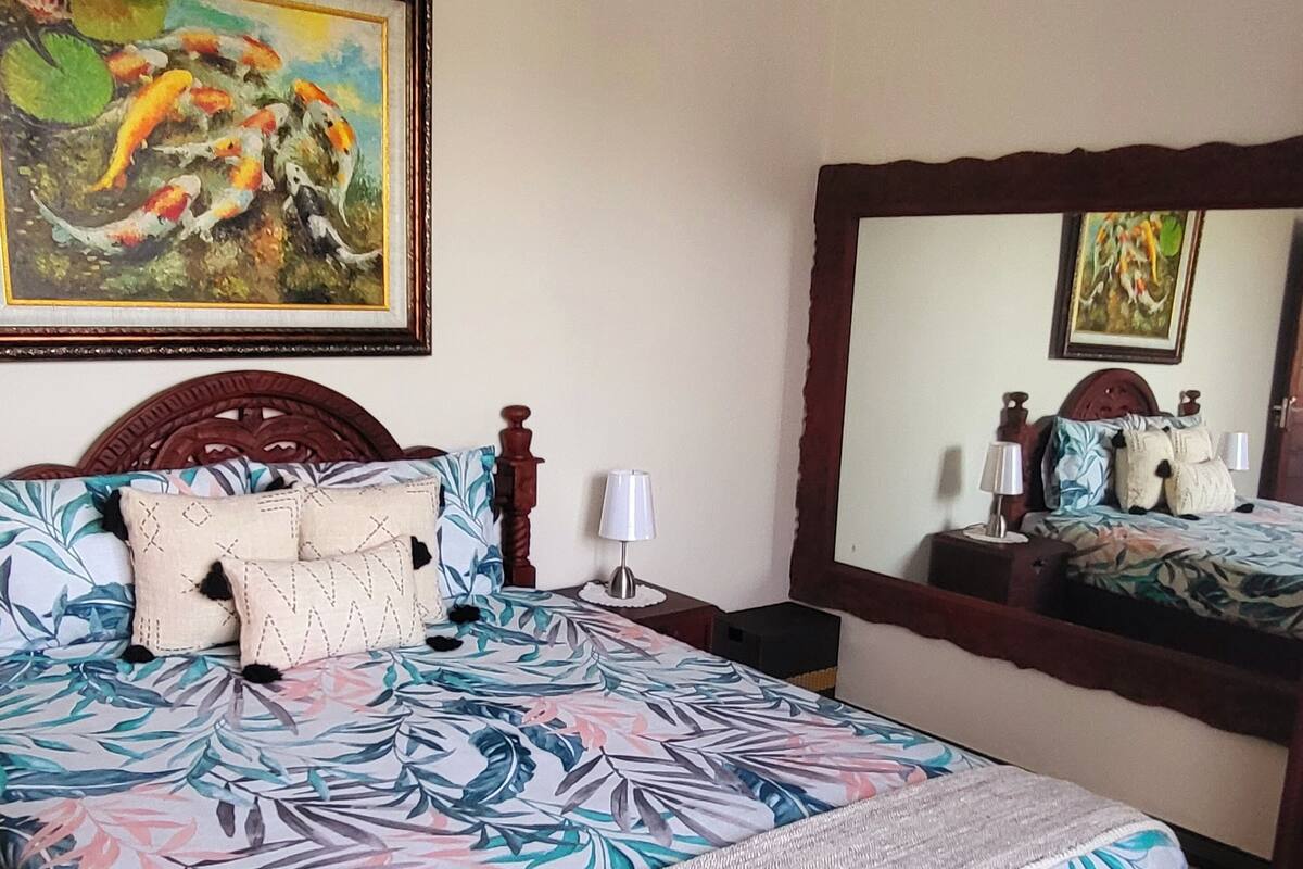 A bedroom with a bed, a nightstand, a dresser, a mirror, and two paintings on the wall.