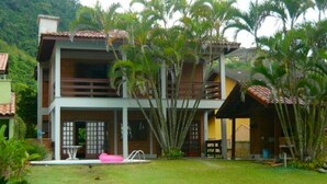 A two-story building with a balcony, surrounded by lush greenery and a swimming pool.