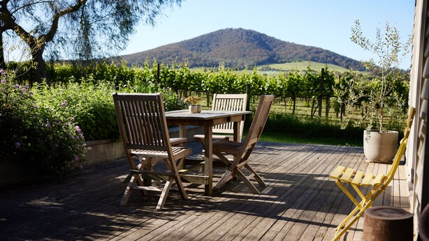 A wooden deck with a table and chairs, a potted plant, and a view of a vineyard and mountain. - Yarra Valley Vineyard Cottage - premier location with spectacular views. (Gruyere)