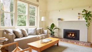 A living room with a fireplace, a sofa, a coffee table, and a bookshelf. - Yarra Valley Vineyard Cottage - premier location with spectacular views. (Gruyere)